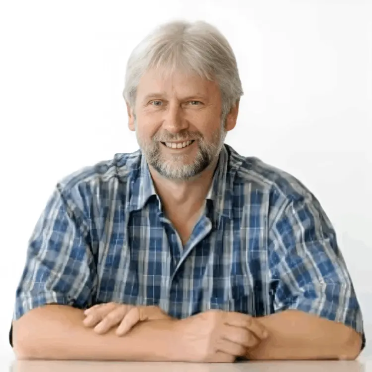 Photo of Ted McGrath, the certified master woodworker and creator of Ted’s Woodworking plans, wearing a blue checkered shirt and smiling